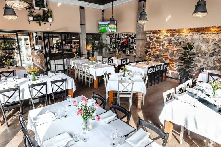 Elegant restaurant dining room with white tablecloths, black and white chairs, fresh floral centerpieces, and exposed stone walls with warm lighting