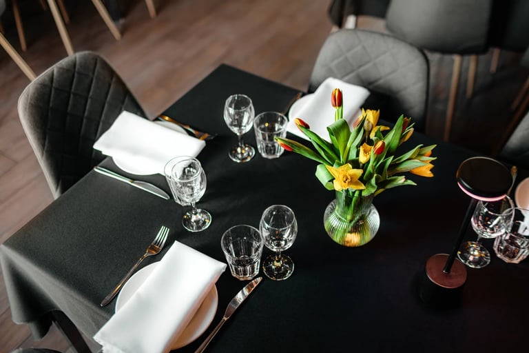 Overhead view of elegant black dining table set with white napkins, glassware, and yellow tulips in a glass vase