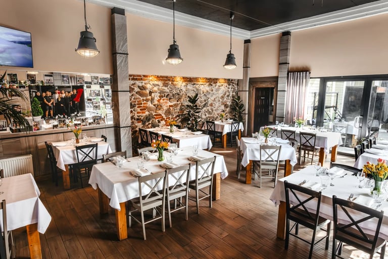 Modern restaurant interior with wooden tables, white tablecloths, pendant lights, and artwork on the walls