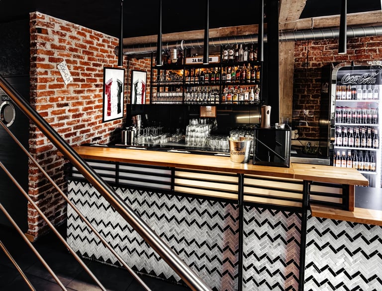 Modern bar counter with chevron patterned front, wooden top, exposed brick walls, and shelves of bottles behind