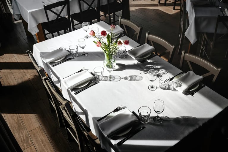 Upscale restaurant dining table set with white linens, place settings, glassware, and red roses in a centerpiece vase