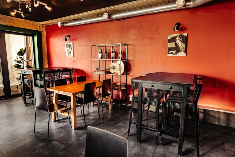 Modern cafe interior with bright orange wall, wooden and black dining tables, chairs, and shelving displays