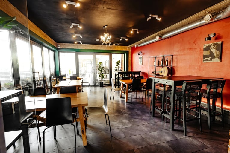Modern restaurant interior with orange walls, black ceiling, wooden tables and chairs, and large windows on the left side